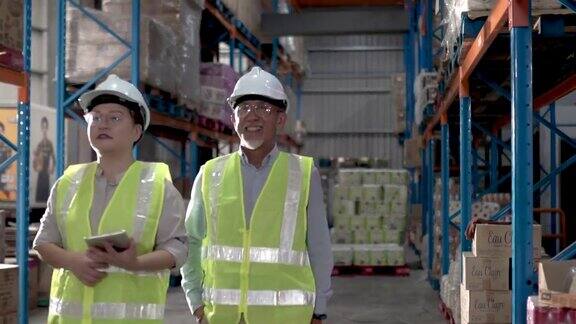 亚洲华人管理库存与仓库工人在仓库与白色安全帽