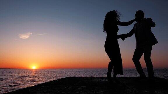 男人和女人在海边夕阳西下跳舞的剪影