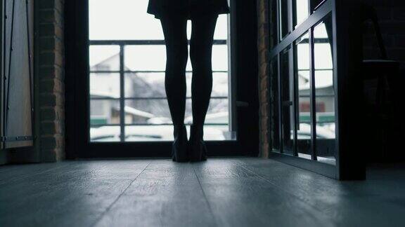 一个穿着黑色靴子的女人走过黑暗的走廊从摄像头到门然后再回来
