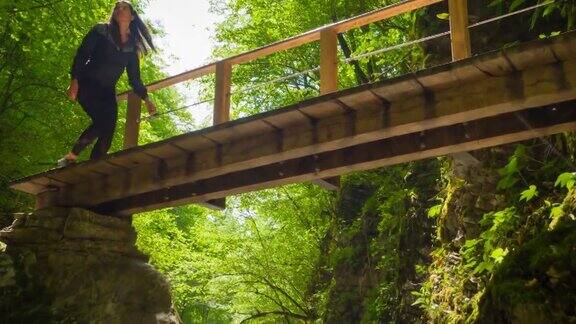 身体有意识的女人徒步穿越木桥在绿色的风景山涧峡谷在一个阳光灿烂的日子