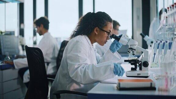医学实验室:美丽的黑人科学家在显微镜下做测试样品的分析多元化的年轻专家团队采用先进的技术设备侧面放大