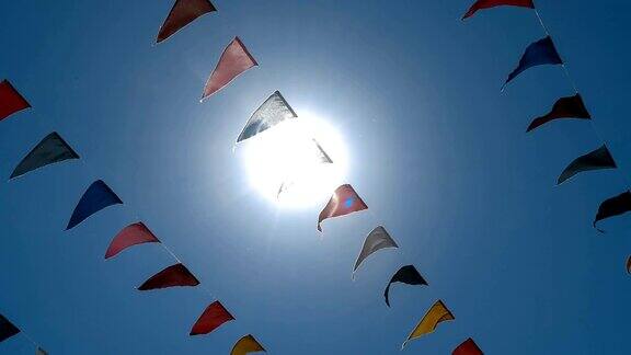 三角形的多彩旗编成的花环在蓝天中迎着阳光摇曳