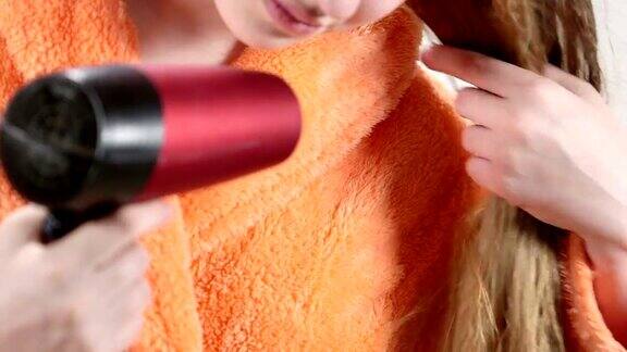 穿着橘色浴袍的年轻女孩用吹风机吹干她湿漉漉的长发