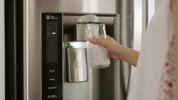 一个女人从家里的冰箱里给水杯装水