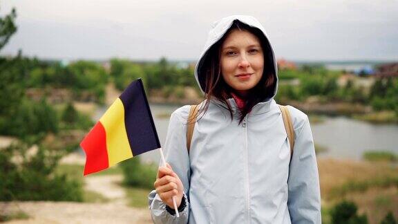 慢动作肖像欢快的游客拿着比利时官方旗帜看着镜头与友好的微笑背景是树木和湖泊的美丽风景