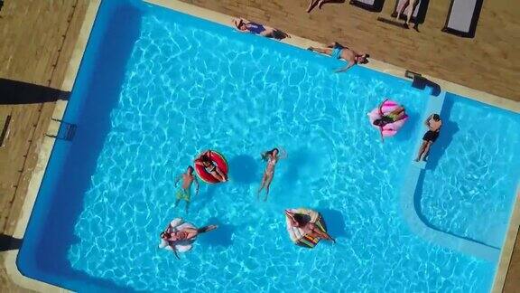 天线朋友们在游泳池里与充气的火烈鸟天鹅床垫一起玩耍在豪华度假胜地快乐的年轻人在漂浮的床垫上沐浴从以上观点穿着比基尼的女孩在阳光下晒日光浴