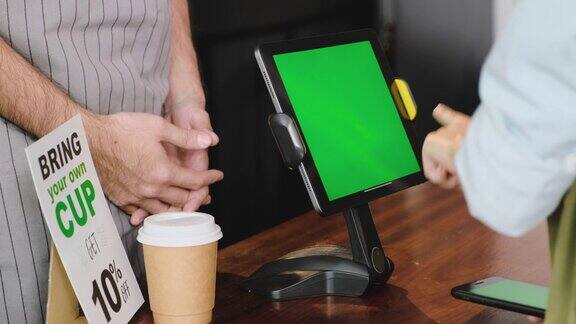 近手顾客在咖啡馆柜台酒吧的绿色屏幕平板电脑菜单上点咖啡