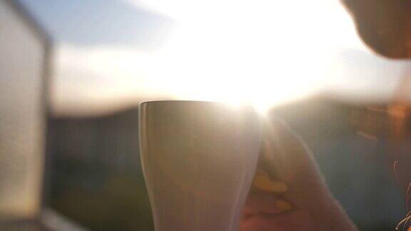 女人在阳台上喝着咖啡欣赏着夕阳慢镜头