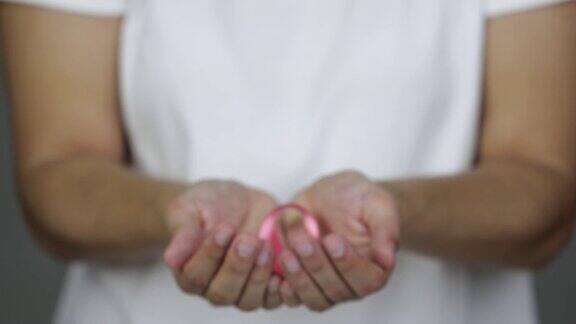 一名妇女向镜头展示了一条粉红色的乳腺癌宣传带