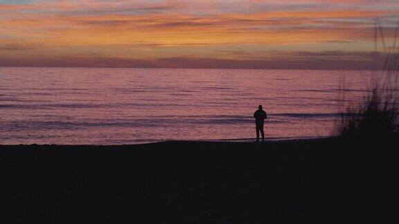 海滩上钓鱼者的鱼竿剪影:冬日的海上夕阳垂钓