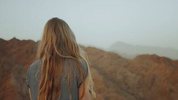 年轻的金发女人穿着长裙走在山顶上山景与日落慢镜头4k