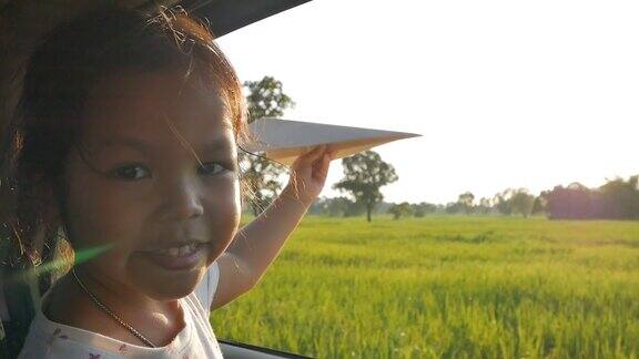 可爱的小女孩在乡下玩着玩具纸飞机窗外晚上放松的活动概念Slowmotion拍摄