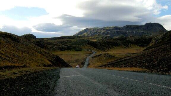 在多云的天气里白色的汽车在风景如画的冰岛山脉之间的公路上行驶