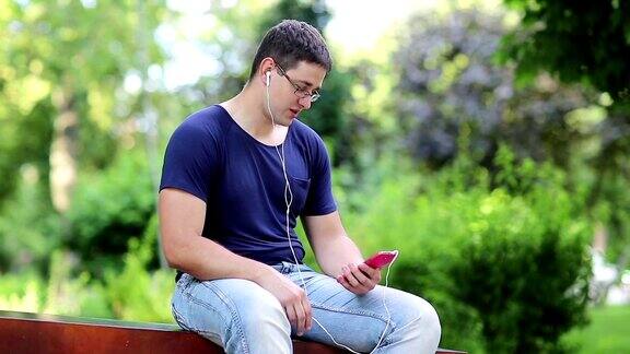 一个年轻人坐在城市公园的长椅上用智能手机说话