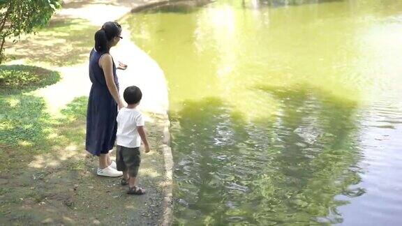 母亲和儿子在公园的池塘里喂鱼食