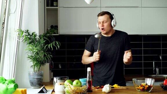 有吸引力的年轻有趣的男子跳舞和唱歌同时在厨房做饭在家