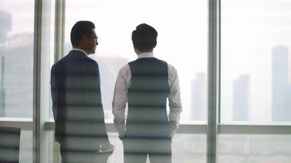 两个亚洲商人站在窗前聊天