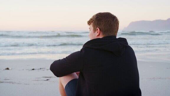 在海滩上看太阳升起的年轻人的后视图
