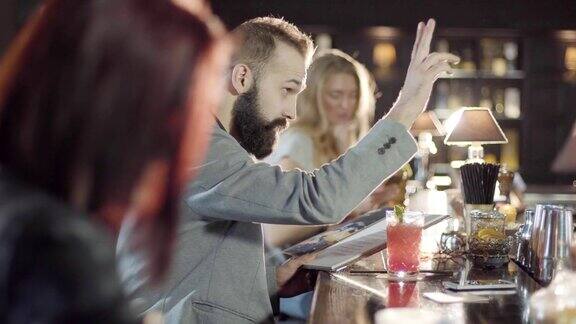 20多岁的大胡子男人坐在吧台上拿着菜单喝鸡尾酒