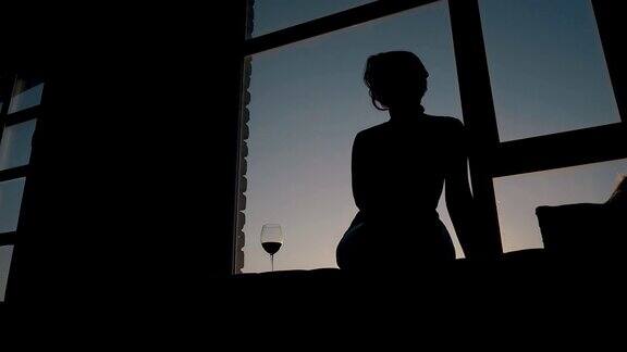 坐在窗台上酒杯旁边的苗条女士的剪影