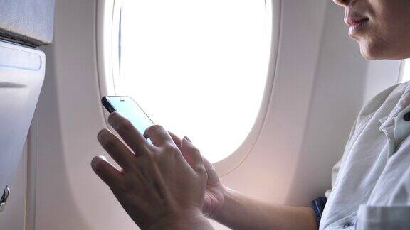 女游客坐在飞机窗口附近在飞行中使用手机
