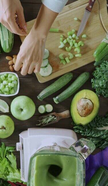 饮食概念:正下方的平移视图拍摄的妇女手切蔬菜为排毒沙冰切菜板和搅拌机放在厨房的桌子上