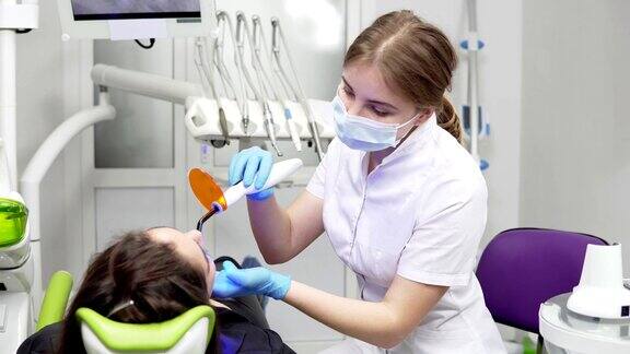 年轻女牙医戴面罩和手套使用牙科紫外线光设备进行聚合物硬化