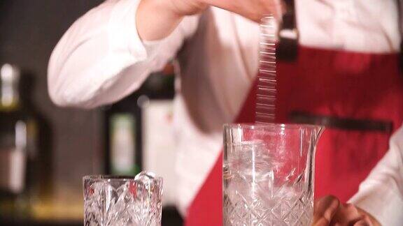 调酒师用长金属勺将冰块和饮料混合在杯子里
