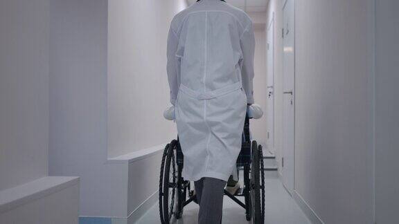 在医院的走廊里一名白人医生推着轮椅带着一个生病的小病人专业儿科医生在医疗诊所帮助男孩的背影画像