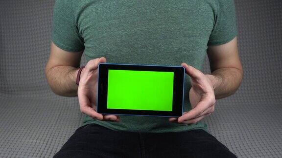 一名男子坐在沙发上用平板电脑显示绿色屏幕的画面