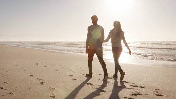 情侣们一起沿着冬季海滩散步的后视图