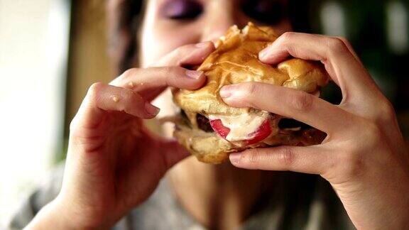 年轻女子咬大美味多汁的汉堡在咖啡馆的特写镜头Slowmotion拍摄