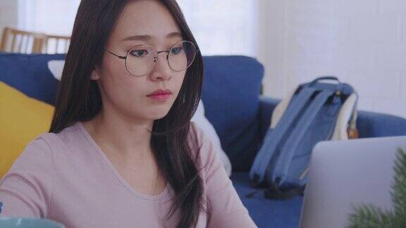 年轻迷人的亚洲女性在家里工作或在笔记本电脑上打字一边喝咖啡一边做生意在家或远程工作的同时在客厅处理多项任务的女性