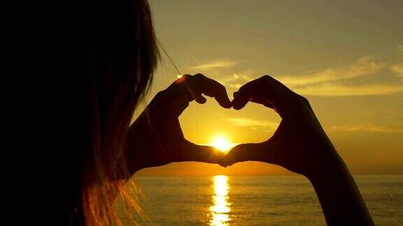 慢镜头:女人用手在夕阳上画出一颗心