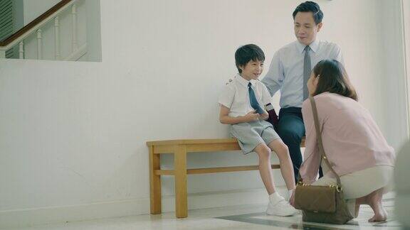 年轻的亚洲母亲正在给她可爱的儿子穿上鞋子而帅气的亚洲父亲坐在长凳上和他的孩子聊天第一天上学准备上学