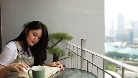 一个亚洲年轻女子在阳台上看书