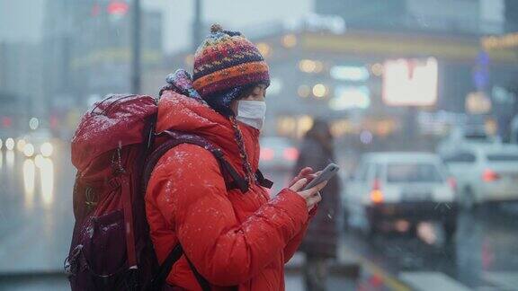 冬天年轻的女游客在城市里用智能手机等待红绿灯