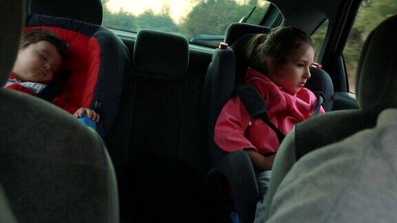小男孩睡在汽车安全座椅上而妹妹试图在公路旅行中小睡