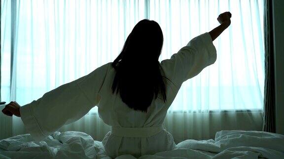 慢镜头FHD亚洲女人早上醒来看着床上的窗户在豪华酒店的卧室生活方式和休闲概念