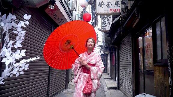 快乐年轻美丽的亚洲女性穿着传统的日本和服手拿红纸伞微笑着走在日本东京新宿地区的街道上