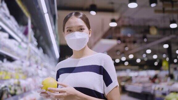 亚洲女性家庭主妇拉着手推车在商场超市挑选商品女性戴着口罩在商场商店里行走寻找消费品