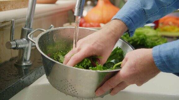 男人在滤锅里洗绿叶蔬菜的特写镜头