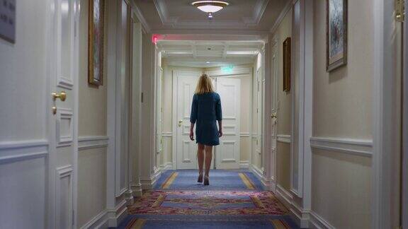 穿着蓝色裙子的年轻女子走在舒适的酒店走廊上