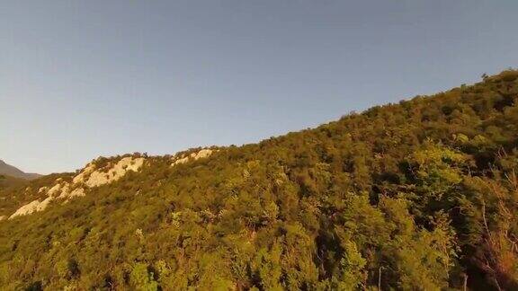 空中电影拍摄高速运动fpv无人机飞越天然的山悬崖峡谷乡村道路包围惊人的自然岩石地形与绿色植被和森林在日落
