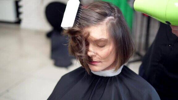 年轻女子在美发沙龙做头发一个男理发师正在用吹风机吹她的头发在4k拍摄