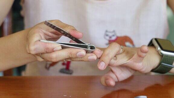 亚洲妇女在家里的木桌上用指甲钳剪指甲