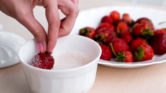 女人把草莓蘸在糖里近距离观察妇女的手旁边的一盘草莓