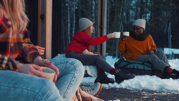 团结快乐的年轻的多民族朋友在舒适的冬季阳台慢动作热饮料杯吐司