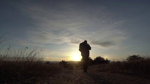 背对着背包看日出的人走在山路上