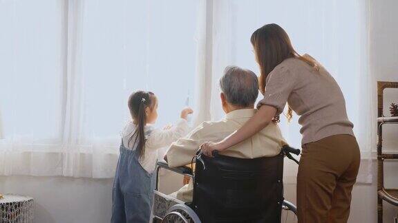 残疾老人坐在轮椅上女儿和孙女微笑着一起玩从窗户里伸出手指